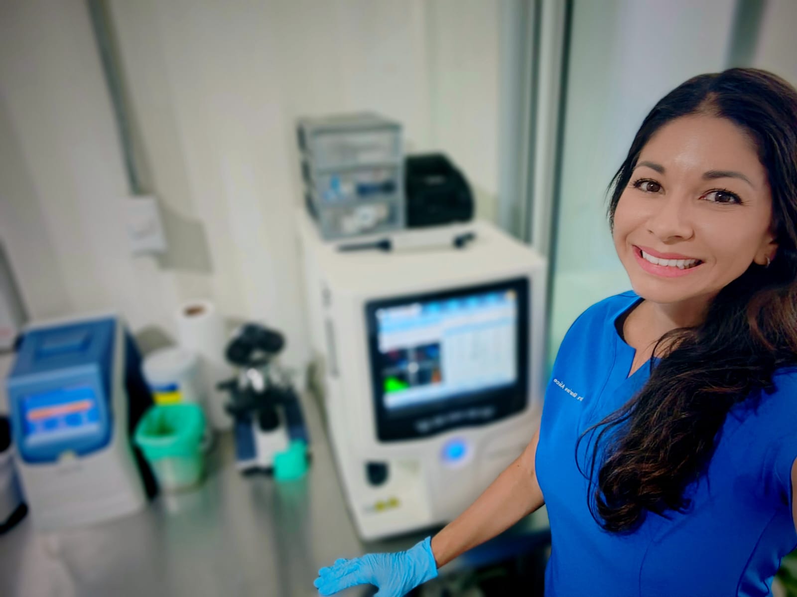Dr. Sharine beside her in-house laboratory analyser, wearing exam gloves
