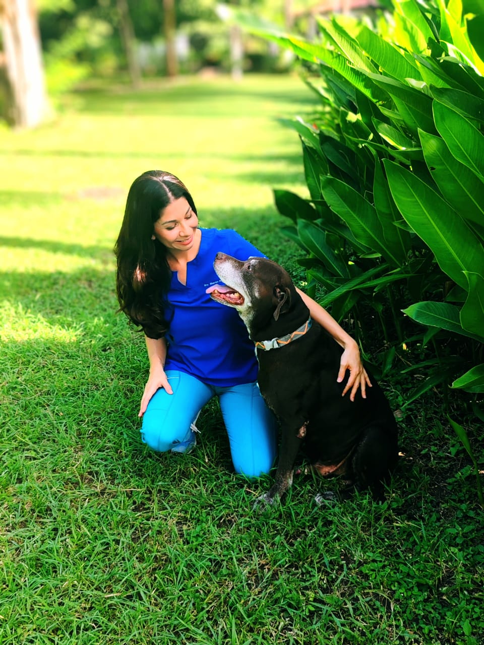 Dr. Sharine kneeling on the grass beside an older black dog